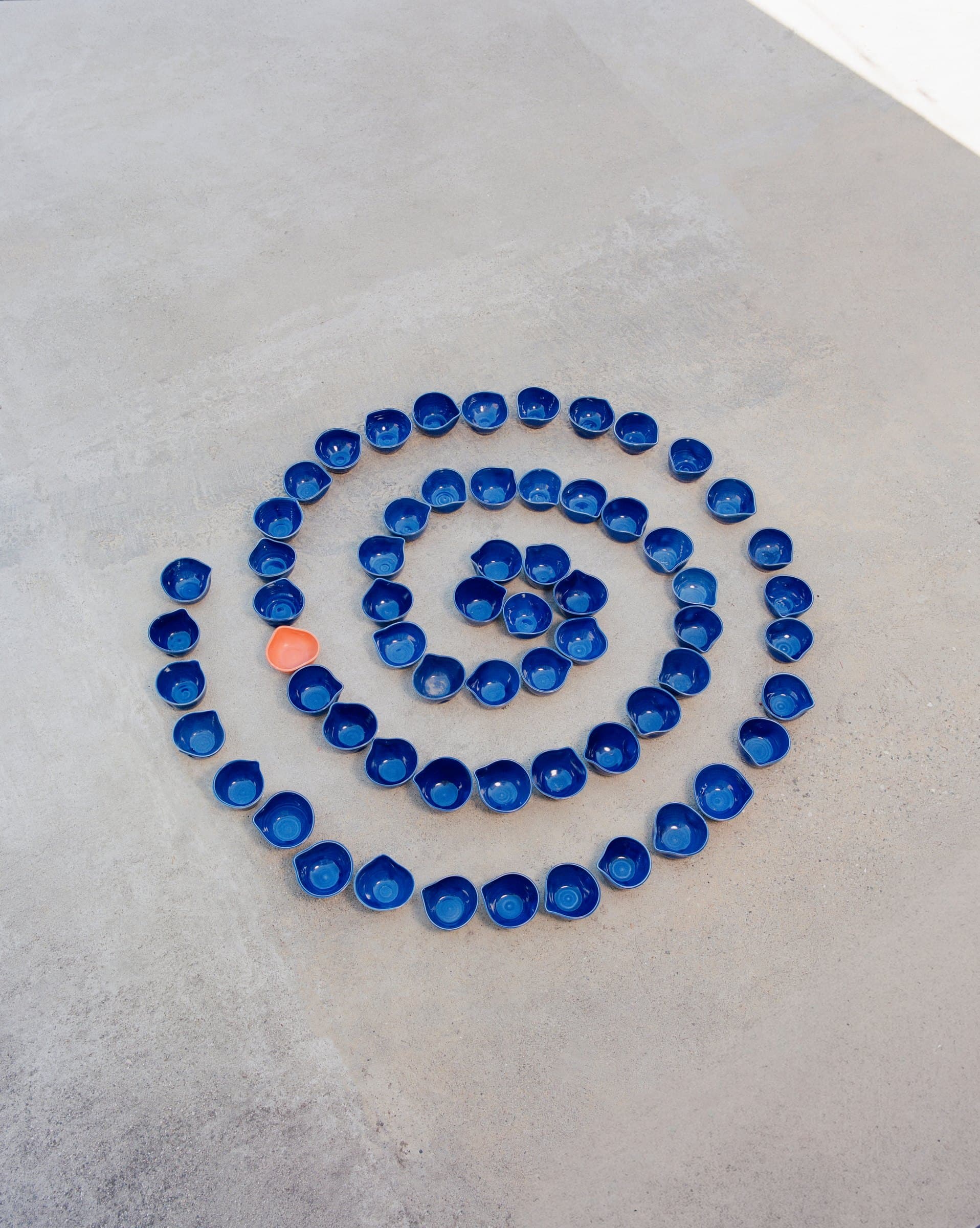 Studio Nia blue spouted bowls arranged in a spiral, one coral bowl among them